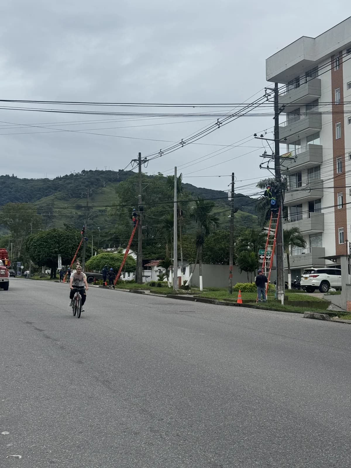 Panorámica de la avenida de Alborada con varias cuadrillas de Voltaje Zero sobre escaleras dieléctricas instalando luminarias LED en los postes, frente a torres residenciales y las montañas de Villavicencio.