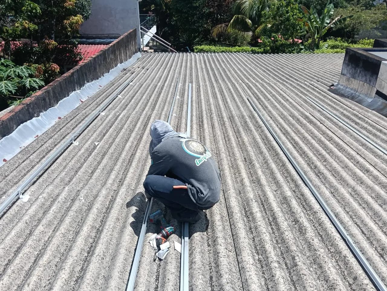 Vista en picado del operario fijando con taladro el riel de aluminio sobre las ondas de la cubierta.