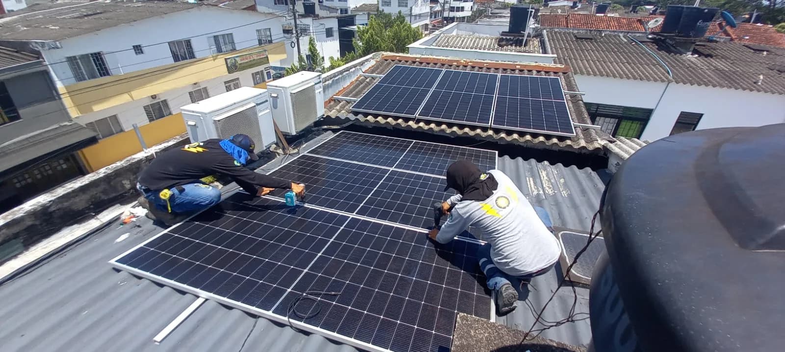 Dos técnicos de la cuadrilla fijando los módulos sobre la cubierta del centro de enseñanza, con el arreglo del alero de teja ya terminado detrás.