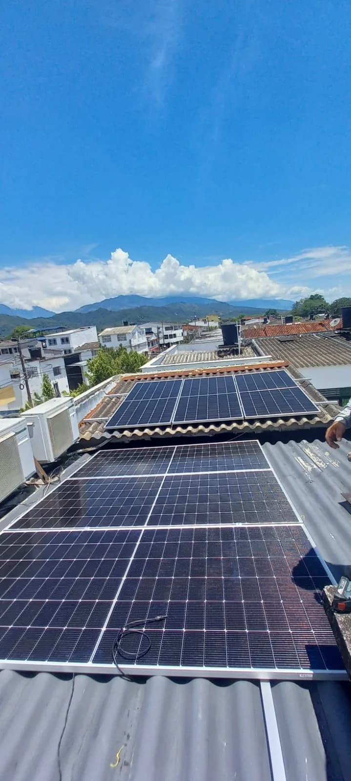 Arreglo solar terminado sobre las dos cubiertas del local, con el barrio y la cordillera al fondo bajo un cielo despejado.