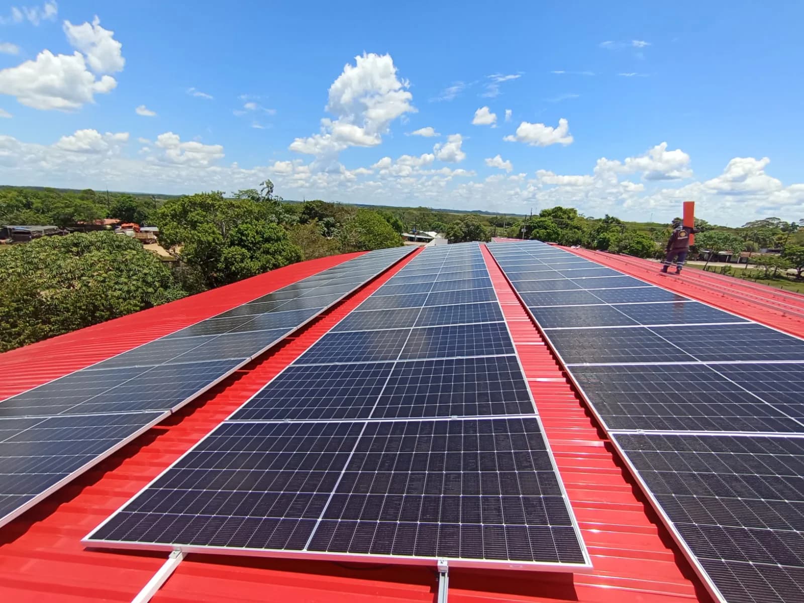 Arreglo solar terminado sobre la cubierta metálica roja de la bodega: tres hileras de módulos convergiendo hacia el horizonte bajo un cielo azul con nubes.