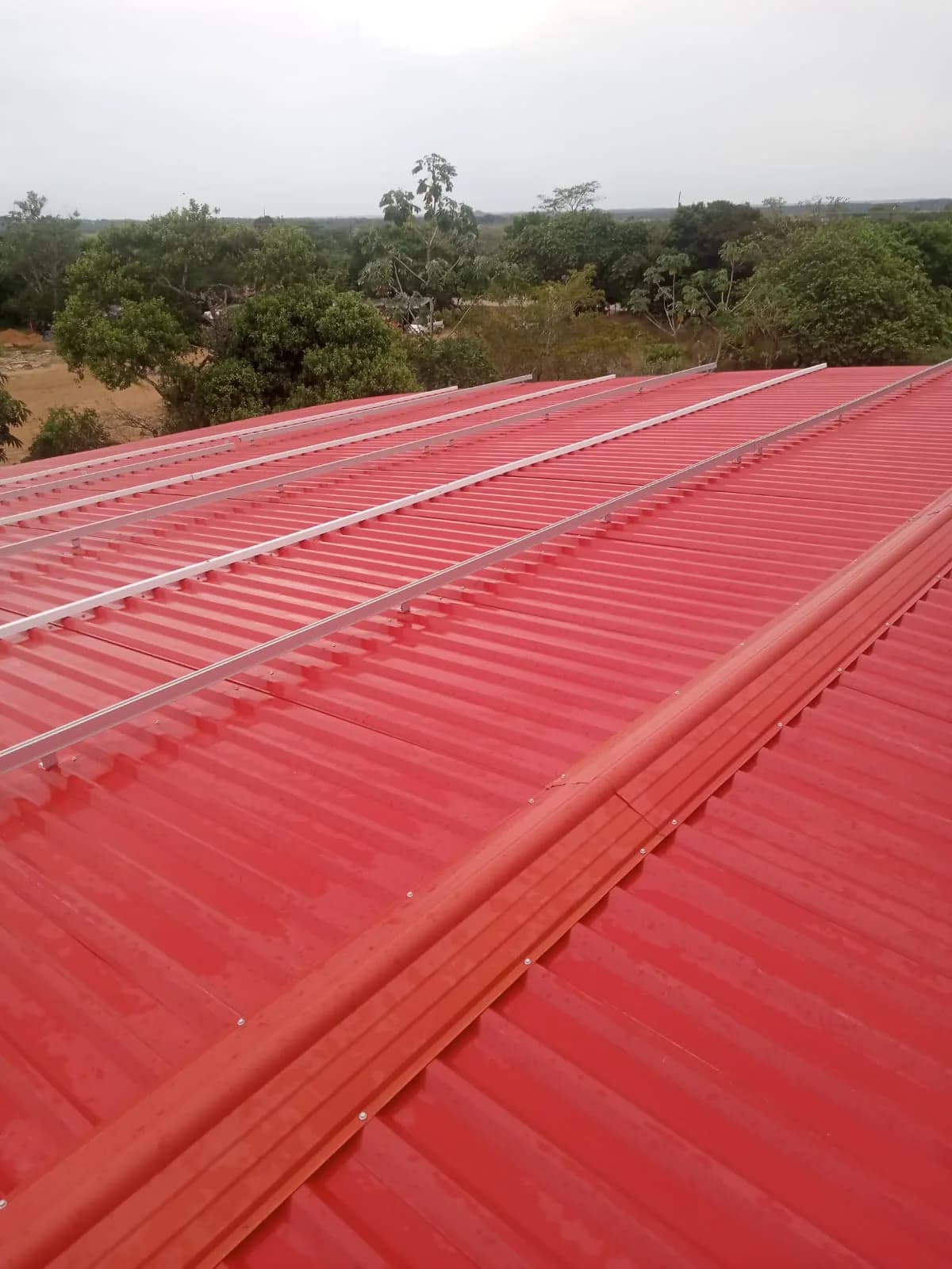 Cubierta metálica roja recién instalada con los rieles de aluminio y los anclajes ya fijados, antes de montar los módulos.