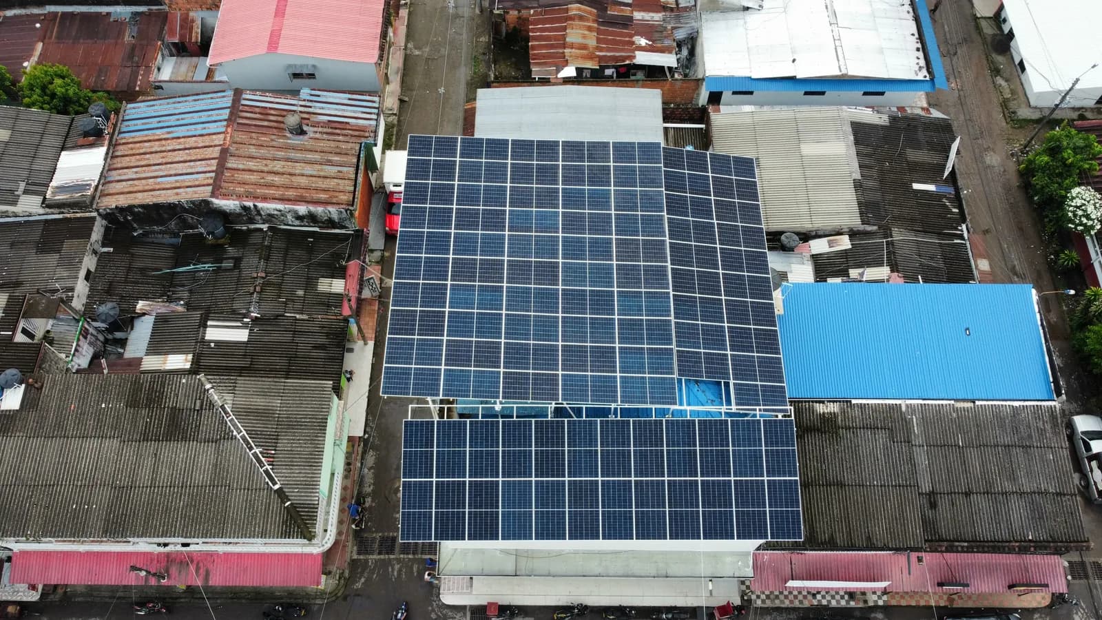Vista cenital con dron de la cubierta del local totalmente ocupada por módulos solares, con la manzana comercial, la vía y el tránsito alrededor.