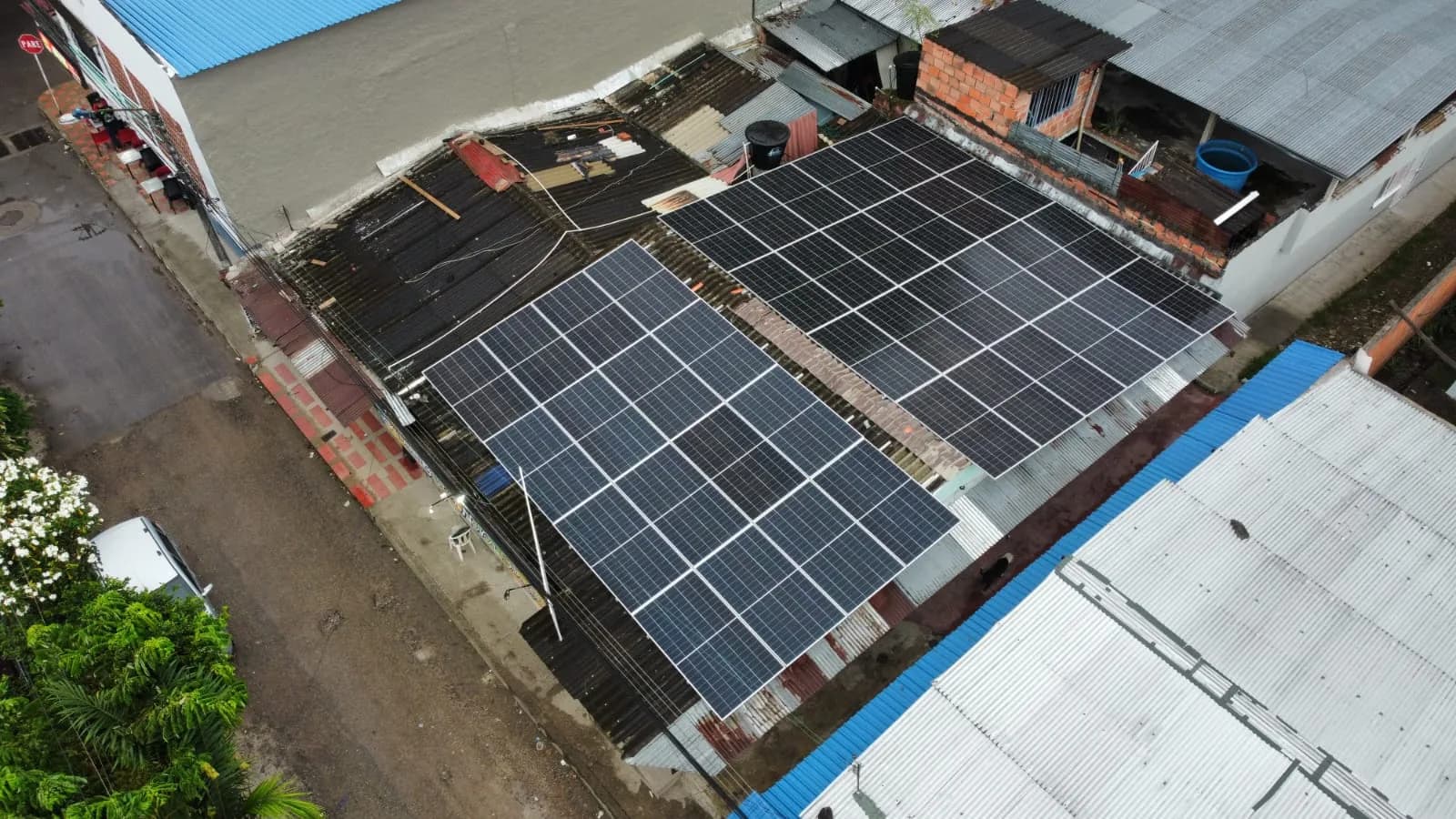 Vista aérea oblicua de los dos bloques de paneles instalados sobre la cubierta, con la calle y las viviendas vecinas.