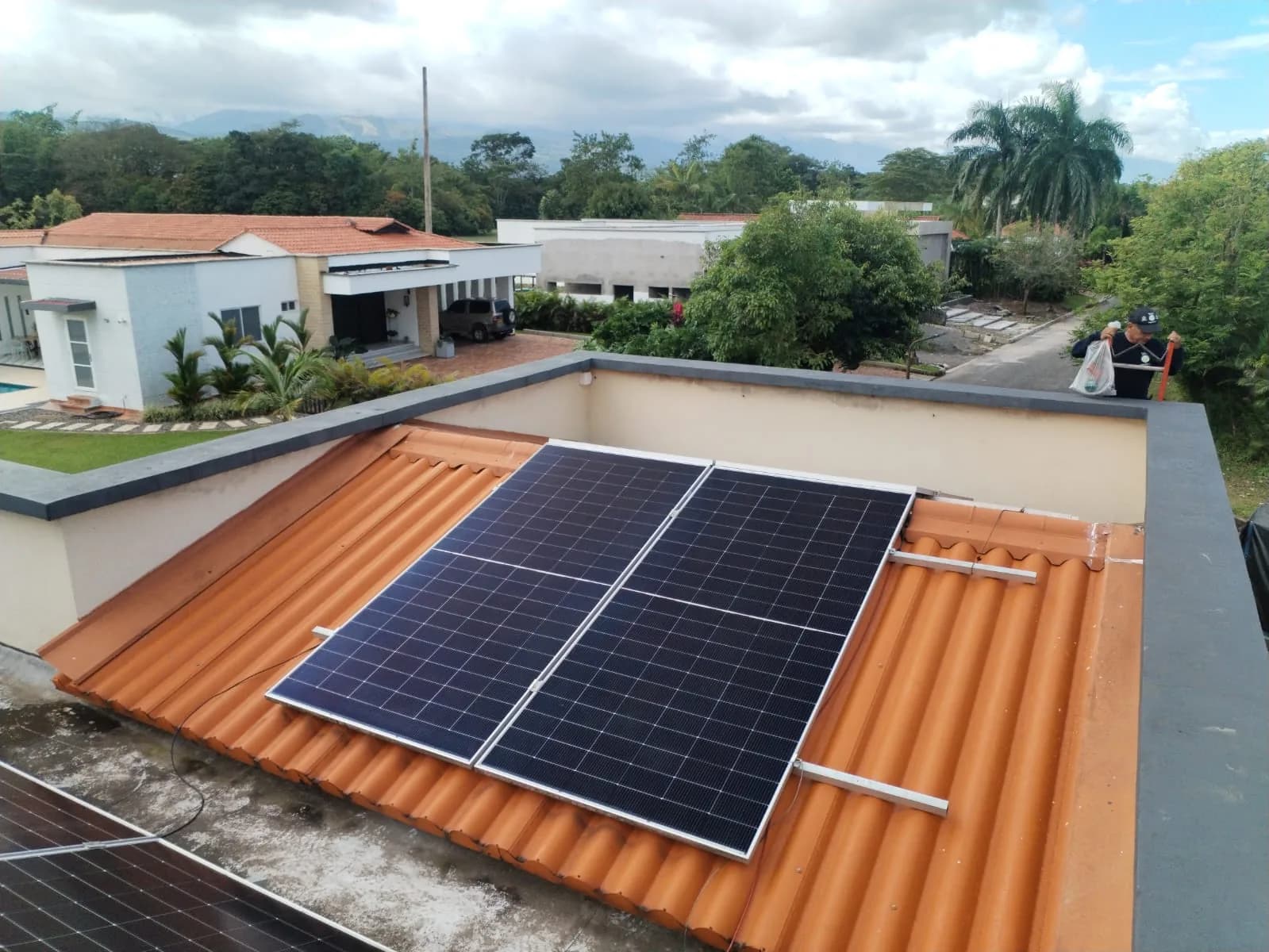 Arreglo solar sobre la cubierta de teja de barro de la casa campestre, con el conjunto de casas vecinas y la cordillera al fondo.