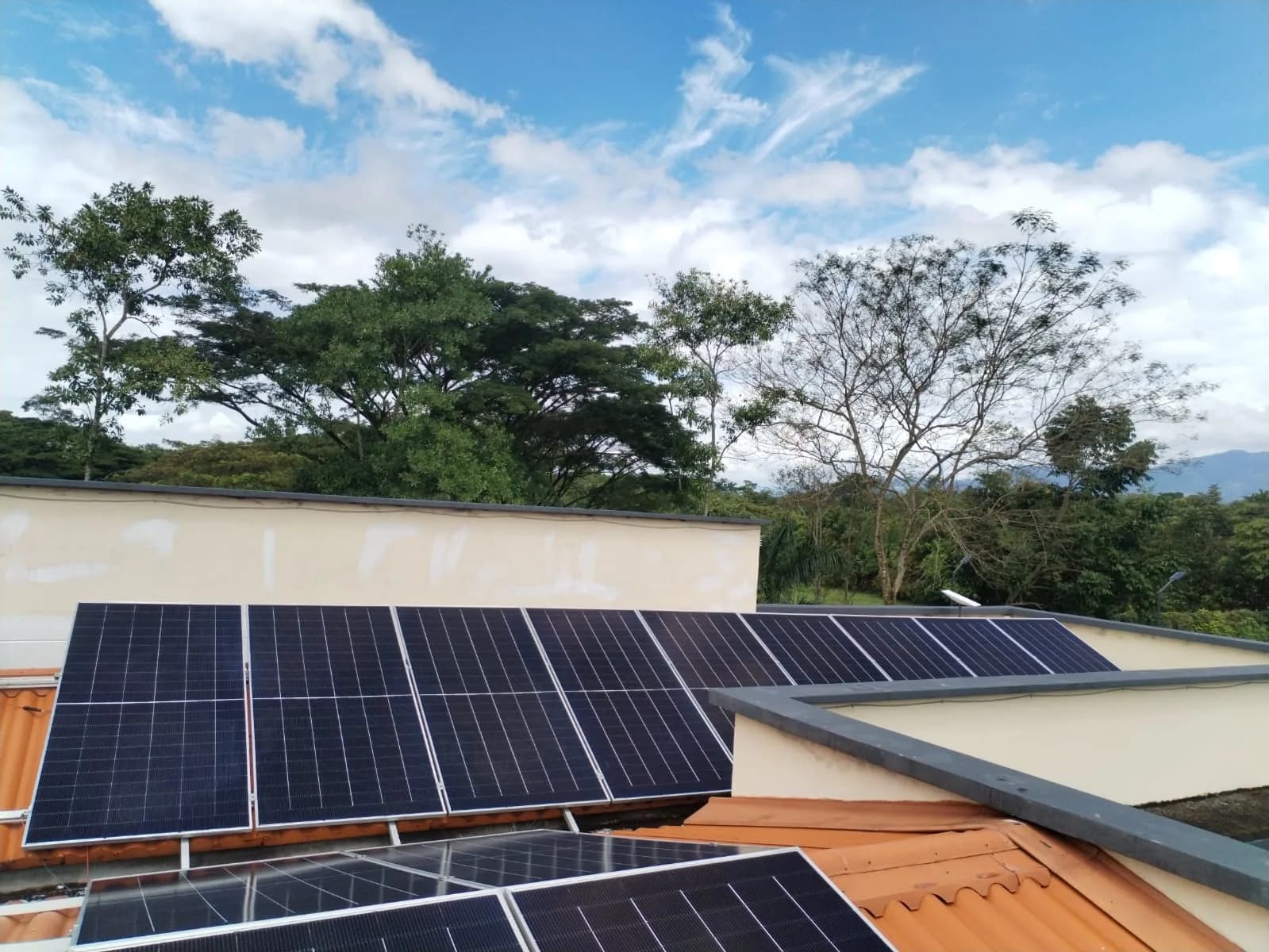 Fila de módulos fotovoltaicos sobre la cubierta recortada contra un cielo azul con nubes altas.