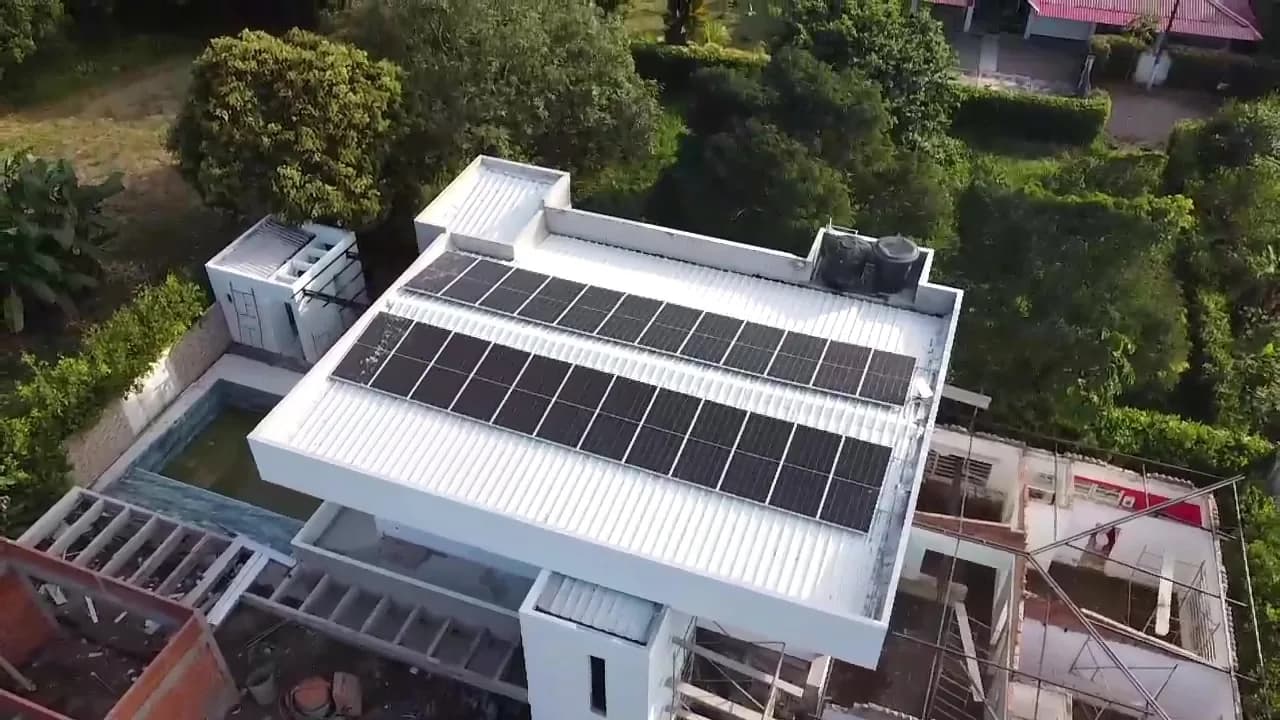 El arreglo fotovoltaico sobre la cubierta blanca visto desde un ángulo más alto, con la piscina, los tanques de agua y el volumen en construcción.