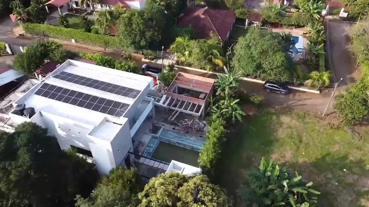 Vista aérea lateral de la vivienda con las filas de paneles en la cubierta, la piscina y la terraza en construcción.