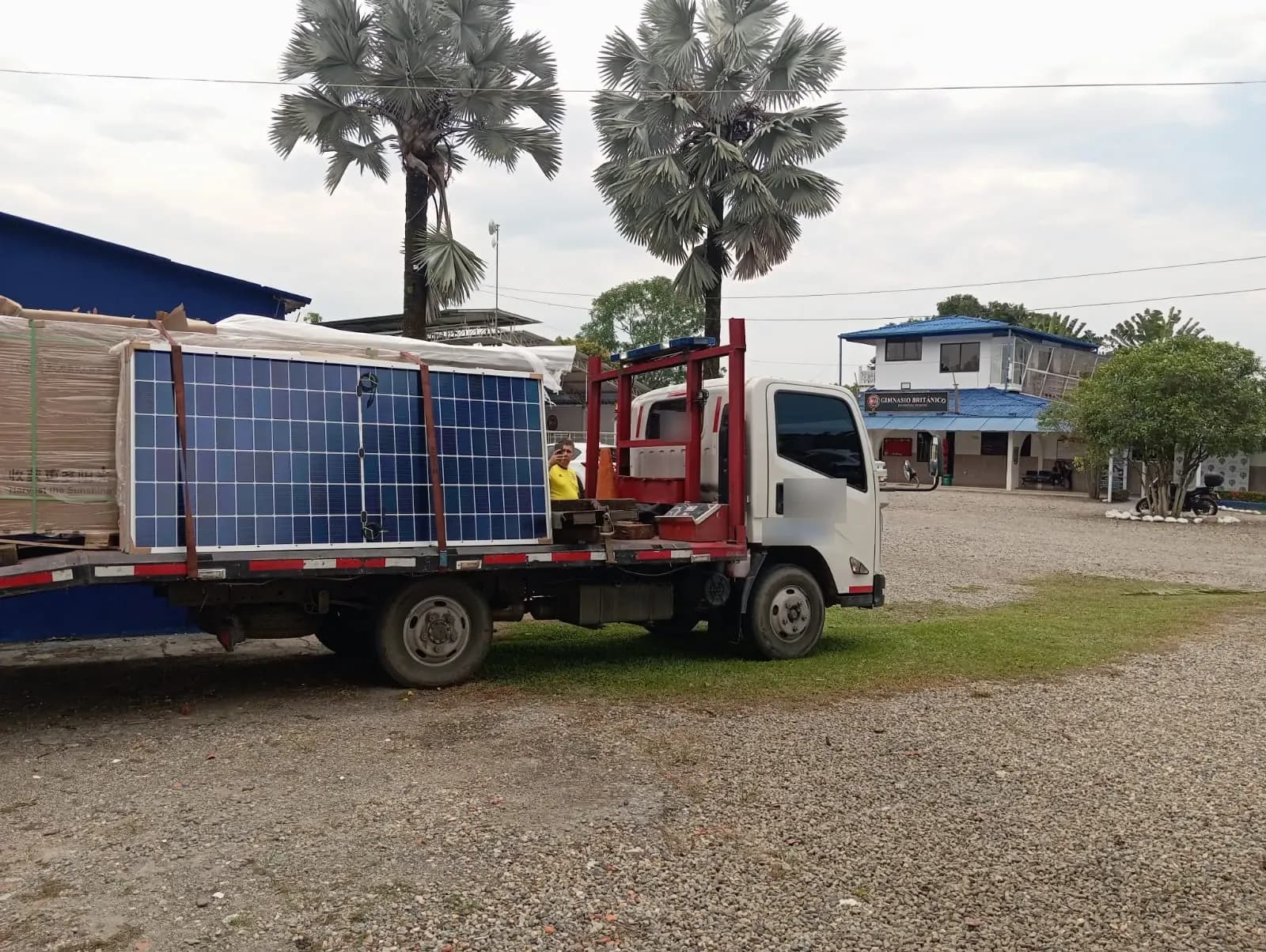 Camión de transporte con estibas de módulos solares llegando al patio del colegio, frente al edificio principal.