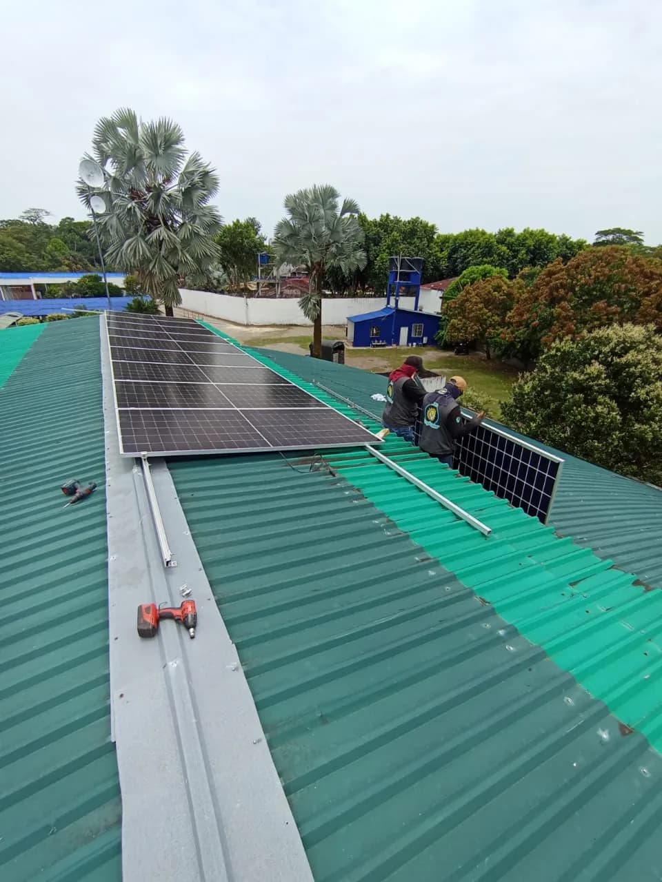 Rieles de aluminio ya fijados sobre la cubierta metálica verde y los primeros módulos montados, con la cuadrilla subiendo un panel y las herramientas sobre el techo.