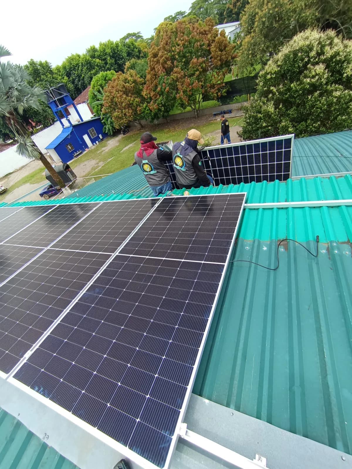 Dos técnicos de la cuadrilla, de espaldas y con chaleco corporativo, ubicando un módulo solar en la última fila de la cubierta.