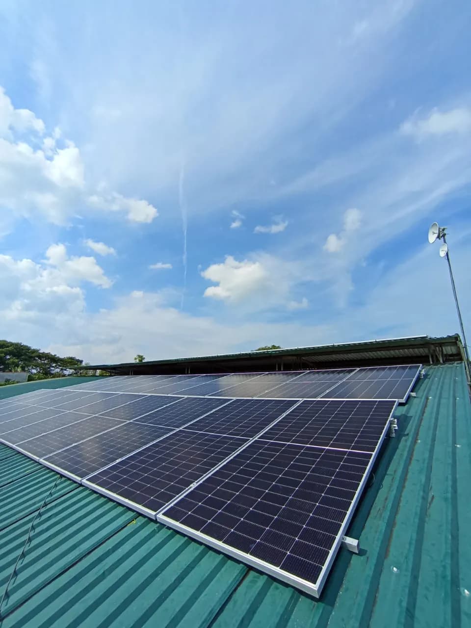 El arreglo solar sobre la cubierta metálica verde recortado contra un cielo azul con nubes.