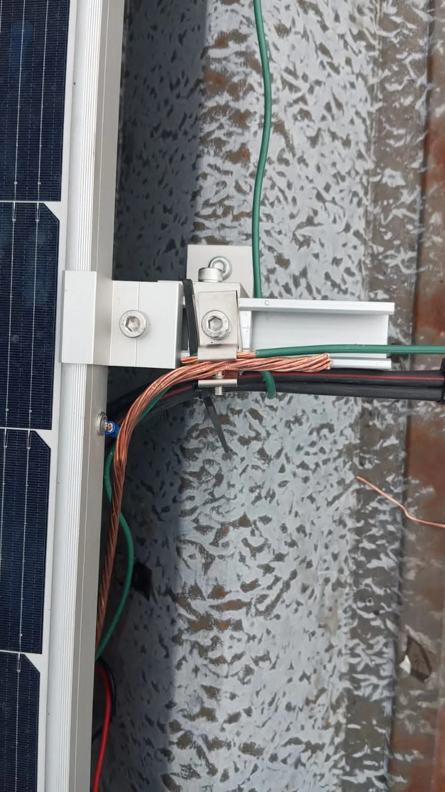 Detalle de la abrazadera intermedia y el conector de puesta a tierra con conductor de cobre desnudo sobre el riel de aluminio.