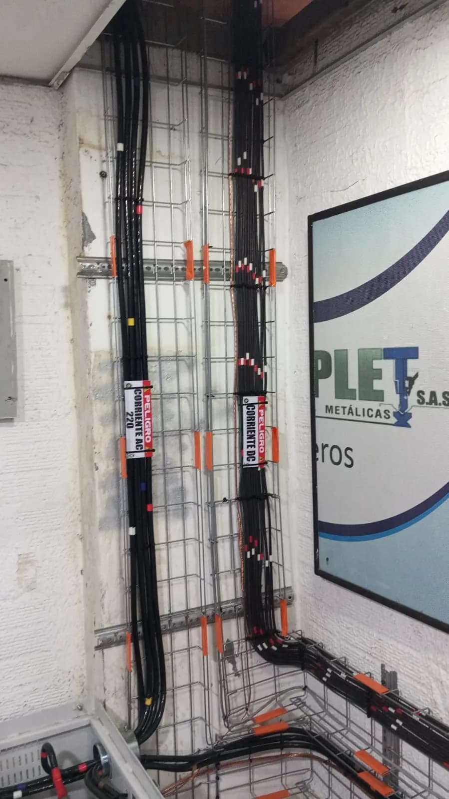 Bandejas portacables verticales con circuitos separados y rotulados PELIGRO CORRIENTE AC 220 y PELIGRO CORRIENTE DC, junto al aviso de Colplet S.A.S.