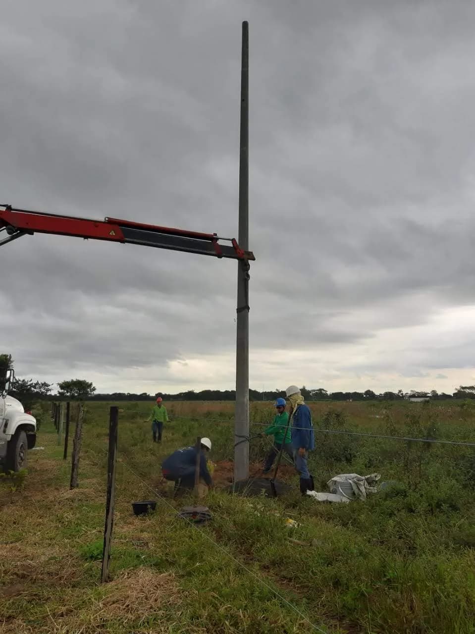 Poste aplomado en su sitio con la cuadrilla compactando el relleno alrededor de la base.