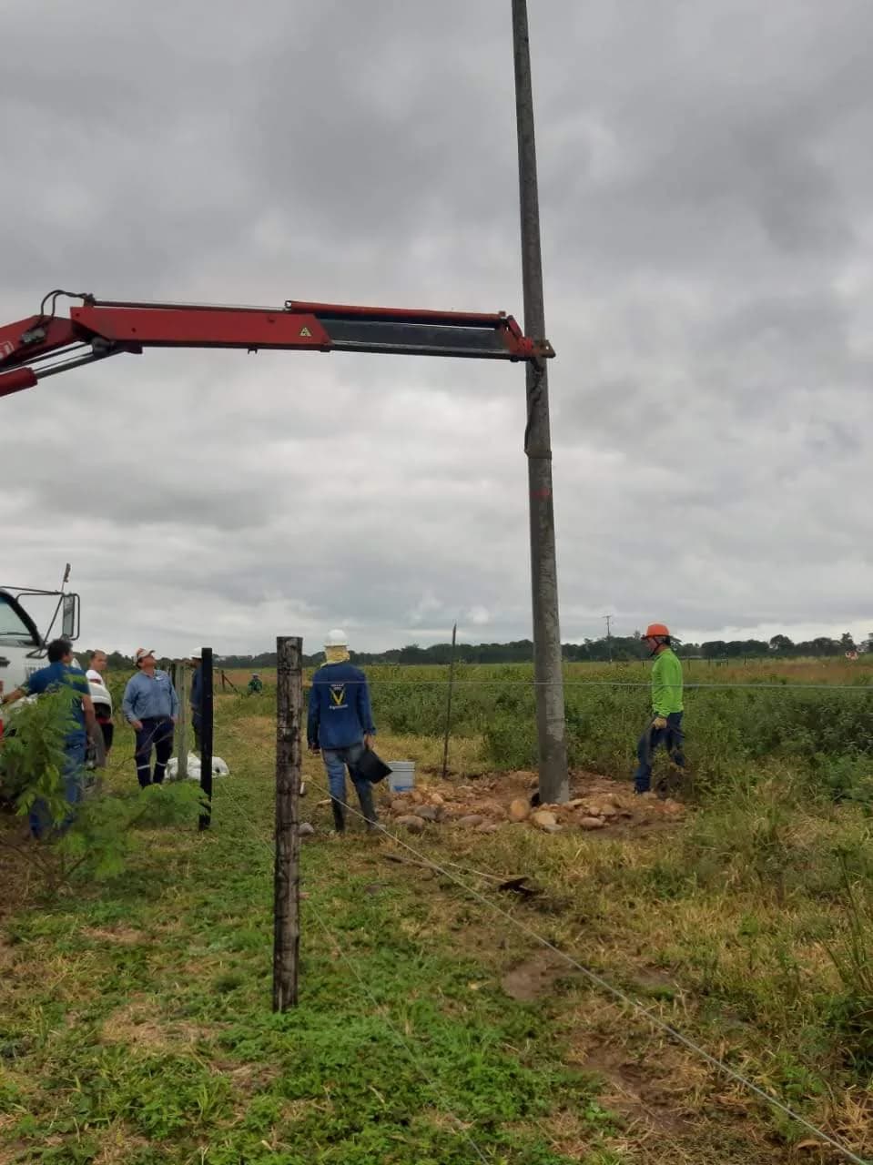 Poste terminado y relleno con piedra, con el personal de Voltaje Zero alrededor y el camión grúa retirándose.
