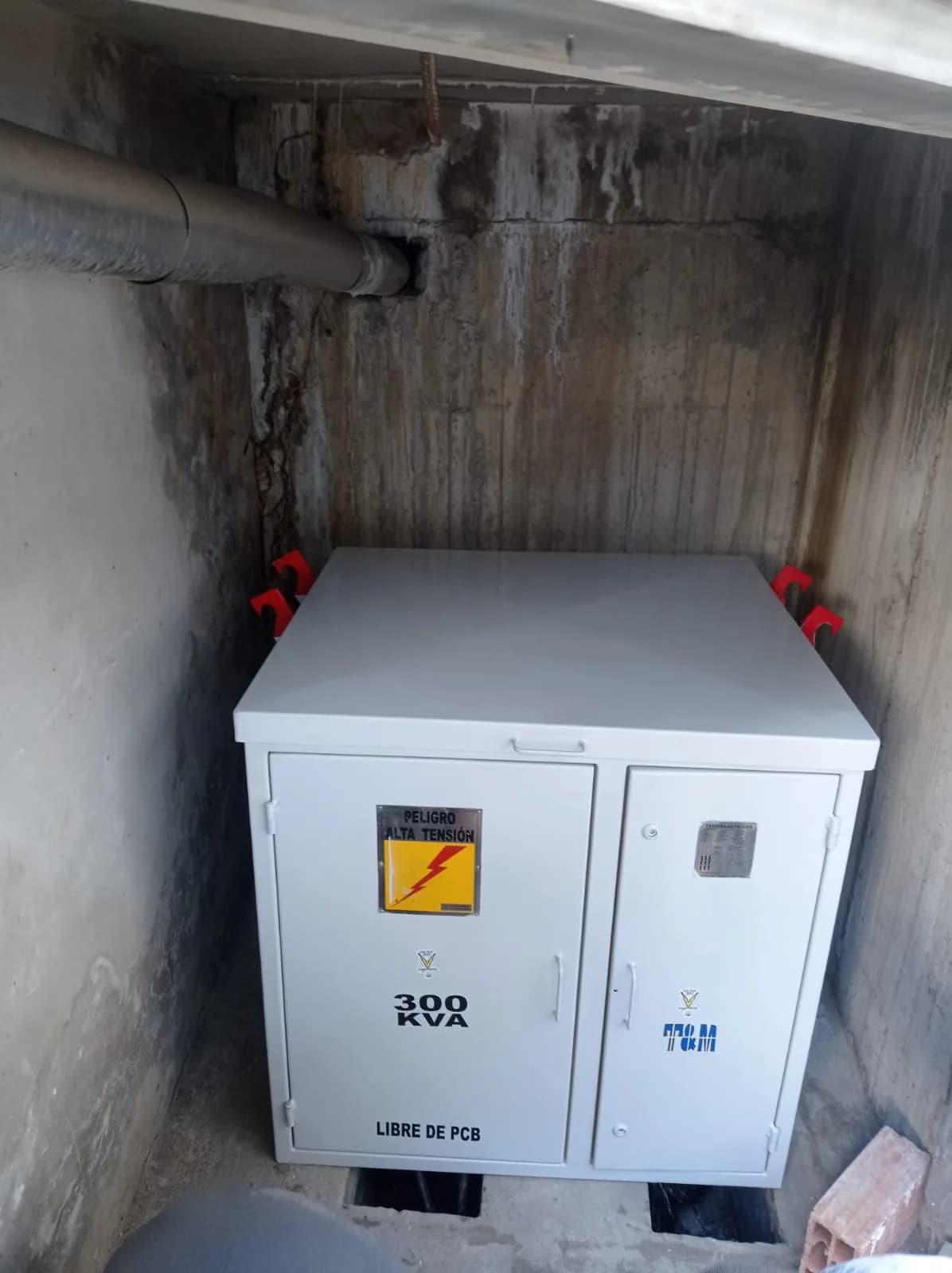 Transformador tipo pedestal de 300 kVA instalado en la bóveda de concreto, con la señalización de alta tensión y la placa de características.