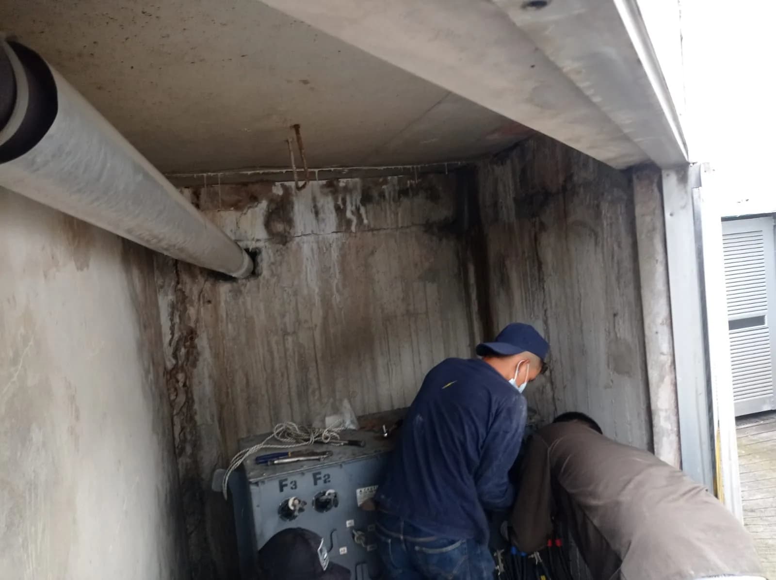 Técnicos desmontando el transformador antiguo, con sus portafusibles y la humedad del cárcamo a la vista.